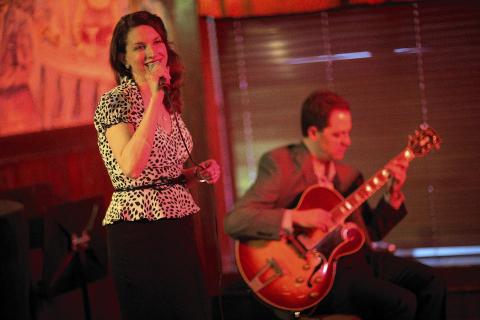 Singer Petra van Nuis stands singing into microphone with guitarist in background