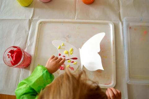 Child adding paint to butterfly cutout