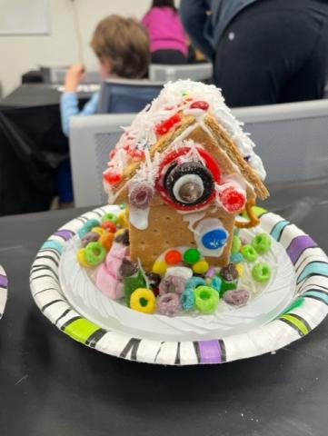 graham cracker gingerbread house on a small white plate. The house is covered in colorful candy and cereal.