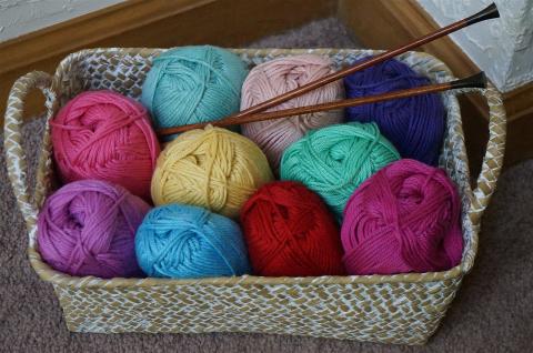 A rectangular basket filled with yarn balls in a wide variety of colors, and two wooden knitting needles.