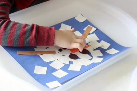 A child making an image of a snowman out of paper cutouts