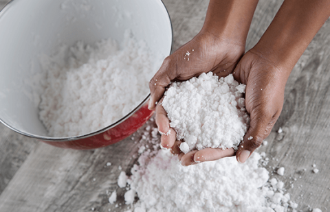 two hands upturned holding fake snow with bowl nearby with more fake snow