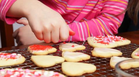 kid in pink shirt putting sprinkles on heart shaped cookies