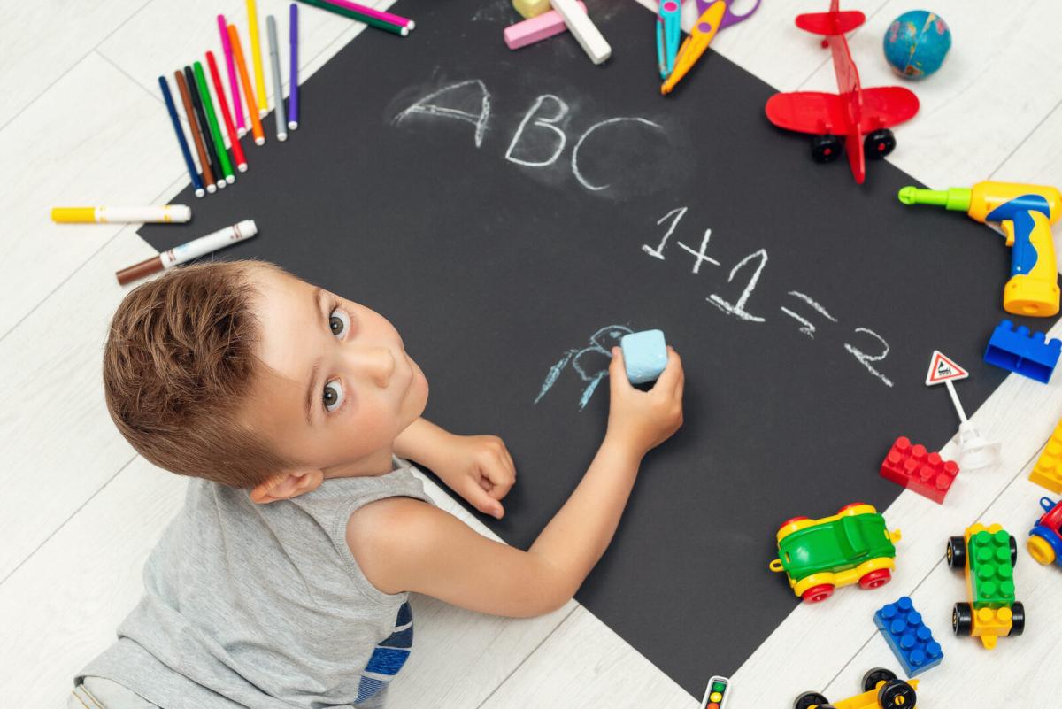 child next to a blackboard practicing his abc's and 123's