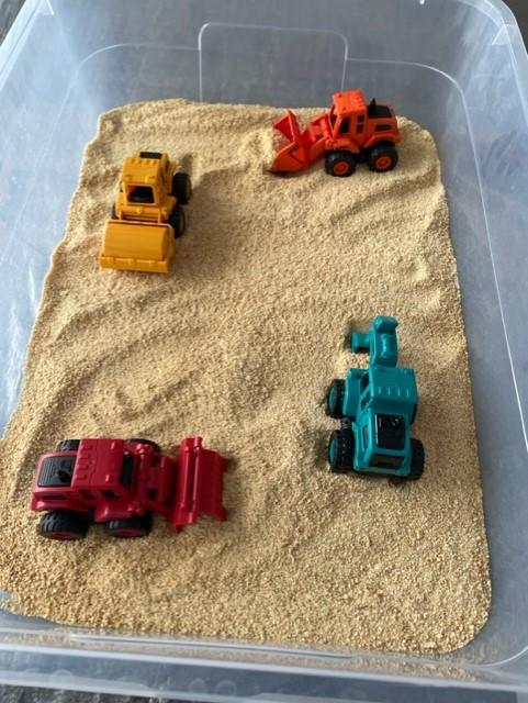 Crushed up graham crackers and colorful construction vehicles in a clear plastic bin