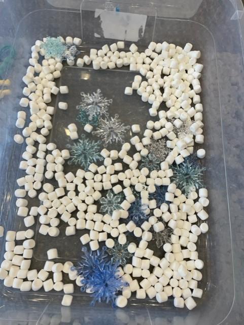 Mini marshmallows and blue and white plastic snowflakes in a clear plastic bin