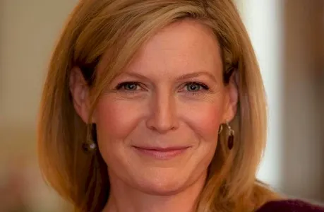 Headshot of Kim Greene Hiller, and blonde blue eyed white woman with medium length hair wearing dangle earrings.