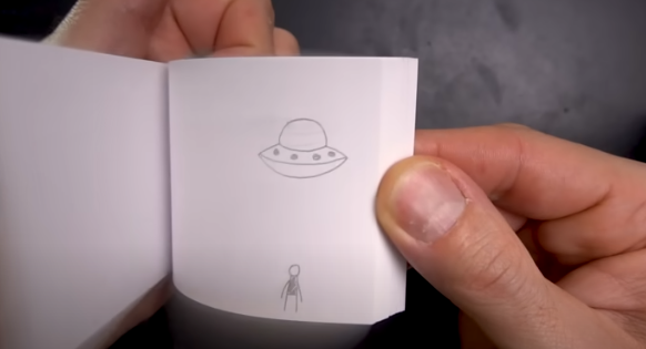 hand holding small page and on the age is drawn spaceship and person